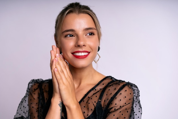 Hermosa mujer impresionante con labios rojos, maquillaje elegante, vestido con glamour negro posando sobre fondo blanco. Evento nocturno.