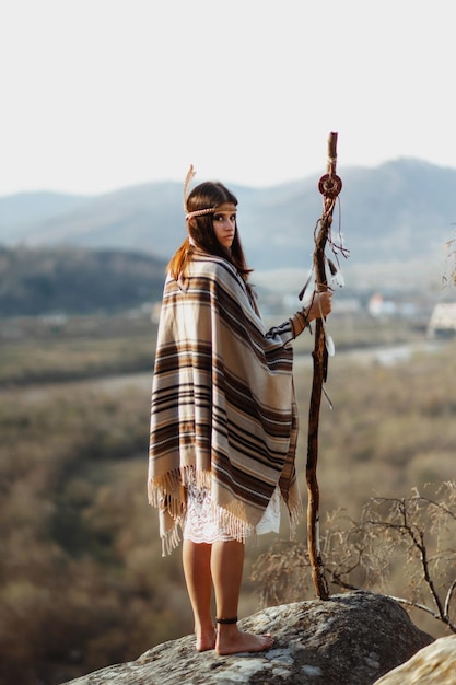 Foto hermosa mujer india americana nativa con chamán guerrero maquillada de pie sobre rocas en el fondo de bosques y ríos