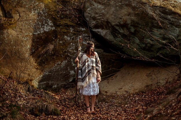Hermosa mujer india americana nativa sosteniendo pikestaff con atrapasueños en el fondo del bosque