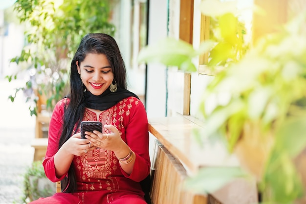 Hermosa mujer india con aplicación de teléfono móvil en la cafetería al aire libre