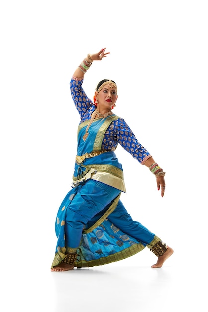 Hermosa mujer india bailando danza tradicional con un elegante vestido azul contra un estudio blanco