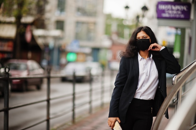 Hermosa mujer india usa una mascarilla formal y negra, posando en la calle durante la pandemia de covid.