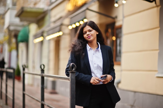 Hermosa mujer india usa una pose formal en la calle con el teléfono móvil en las manos