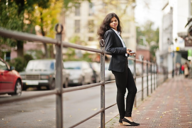 Hermosa mujer india usa una pose formal en la calle con el teléfono móvil en las manos