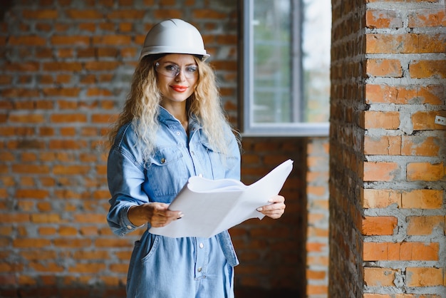 Hermosa mujer ingeniera está revisando los planos de una obra de construcción