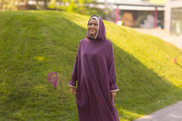 Hermosa mujer islámica en un vestido musulmán de pie en un parque de verano, fondo de la calle, bosque, otoño, árboles. Día mundial del hijab.