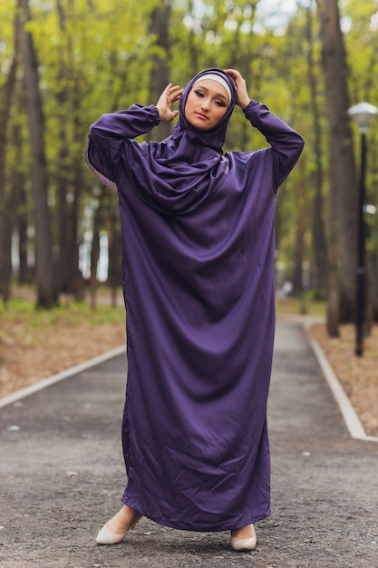 Hermosa mujer islámica en un vestido musulmán de pie en un parque de verano, fondo de la calle, bosque, otoño, árboles. Día mundial del hijab.