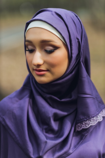 Hermosa mujer islámica en un vestido musulmán de pie en un parque de verano, fondo de la calle, bosque, otoño, árboles. Día mundial del hijab.