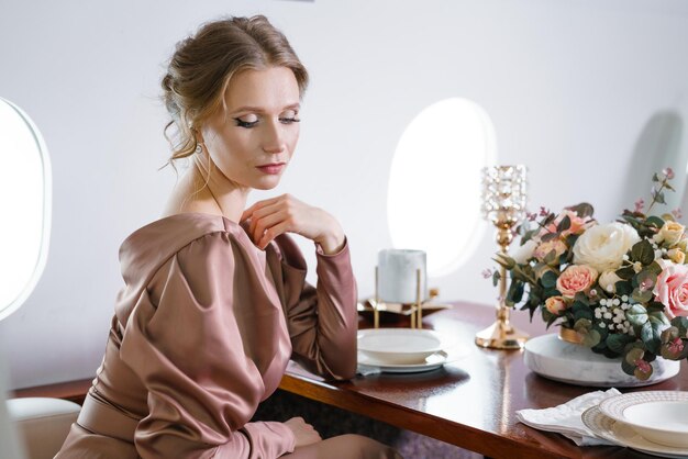 Hermosa mujer en jet privado con elegante vestido con peinado y maquillaje se sienta en la mesa festiva con...