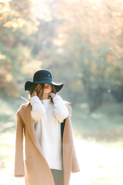 Hermosa mujer joven con abrigo y sombrero negro en el parque