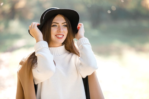 Hermosa mujer joven con abrigo y sombrero negro en el parque