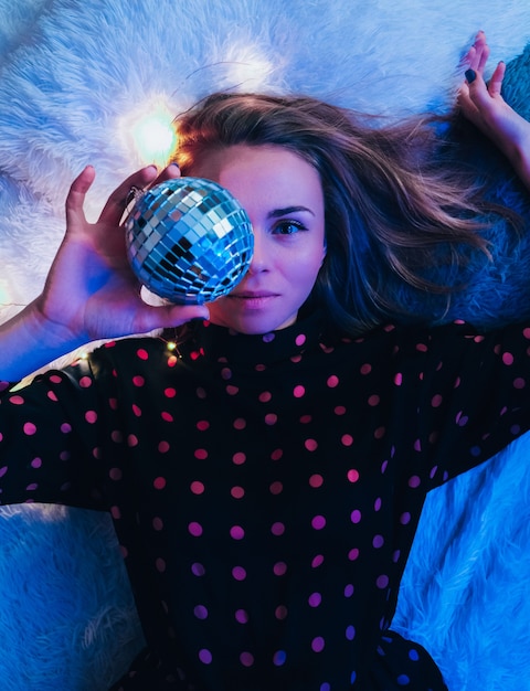 Hermosa mujer joven acostada con bola de discoteca. Concepto de fiesta. Año nuevo navidad o fiesta de cumpleaños. Felices alegres y sueños mágicos. Divirtiéndose