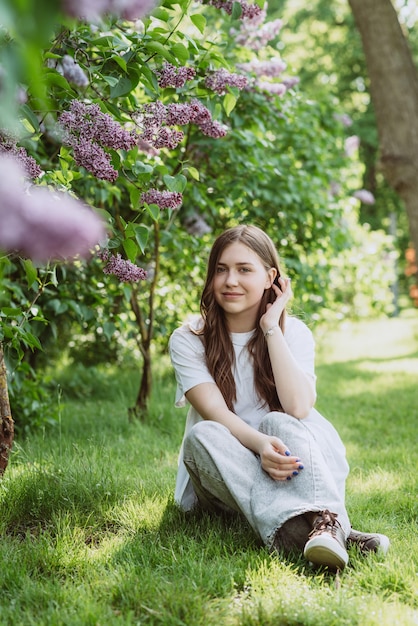 Hermosa mujer joven, adolescente, cerca de un arbusto lila en un parque soleado de primavera. Enfoque selectivo suave.