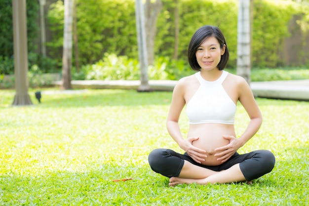 Hermosa mujer joven asiática embarazada relajarse en el parque.
