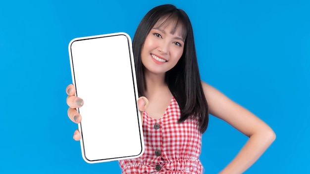 Hermosa mujer joven asiática Emocionada chica sorprendida mostrando un gran teléfono inteligente con pantalla en blanco para publicidad de aplicaciones móviles aislada en la pantalla del teléfono inteligente de fondo azul Imagen simulada