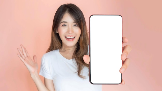 Hermosa mujer joven asiática que muestra un gran teléfono inteligente con pantalla en blanco espacio de copia vacío de pantalla blanca para banner publicitario aislado en fondo rosa Imagen de maqueta