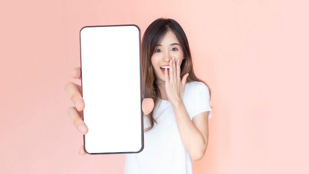 Hermosa mujer joven asiática que muestra un gran teléfono inteligente con pantalla en blanco espacio de copia vacío de pantalla blanca para banner publicitario aislado en fondo rosa Imagen de maqueta