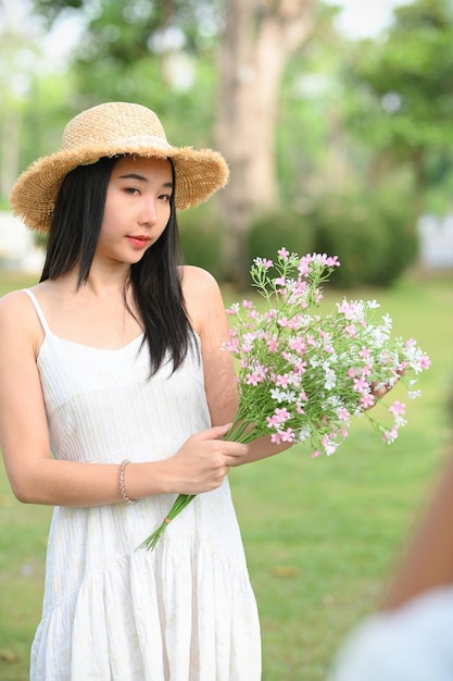 Hermosa mujer joven asiática con un ramo de flores de pie en un jardín verde