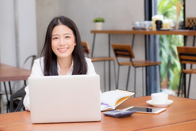 Hermosa mujer joven asiática trabajando en línea en la computadora portátil sentado en la cafetería.