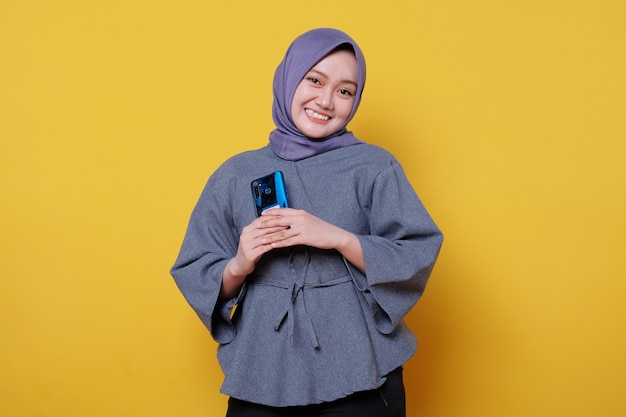 Hermosa mujer joven de aspecto amable positivo con hijab con hermosa sonrisa sincera sintiéndose agradecida y agradecida sosteniendo el teléfono móvil
