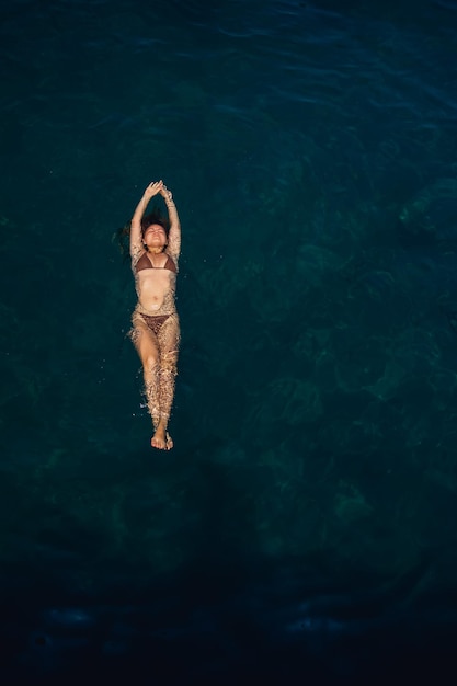 Foto una hermosa mujer joven y atractiva en traje de baño se encuentra en la superficie del agua en el mar vista desde arriba ella está disfrutando de sus vacaciones enfoque selectivo