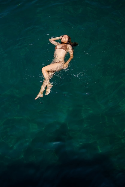 Una hermosa mujer joven y atractiva en traje de baño se encuentra en la superficie del agua en el mar. Vista desde arriba. Está disfrutando de sus vacaciones. Enfoque selectivo