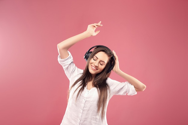 Hermosa mujer joven en auriculares inalámbricos escuchando música y bailando