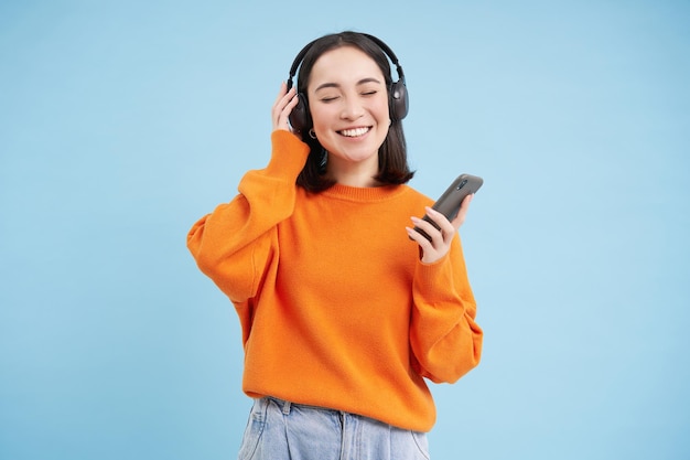 Hermosa mujer joven en auriculares con teléfono móvil escucha música en auriculares y sonríe azul