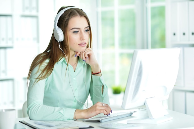 Hermosa mujer joven con auriculares trabajando con computadora