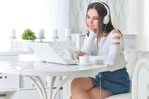 Hermosa mujer joven en auriculares usando laptop en casa