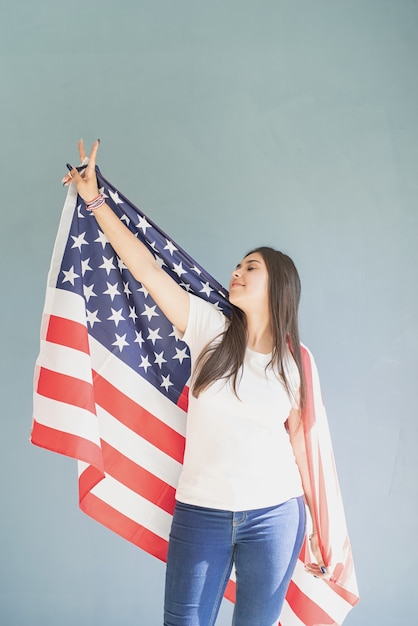 Hermosa mujer joven con bandera americana sobre fondo azul.