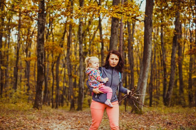 Hermosa mujer joven con bebé en el bosque recoge el brashwood