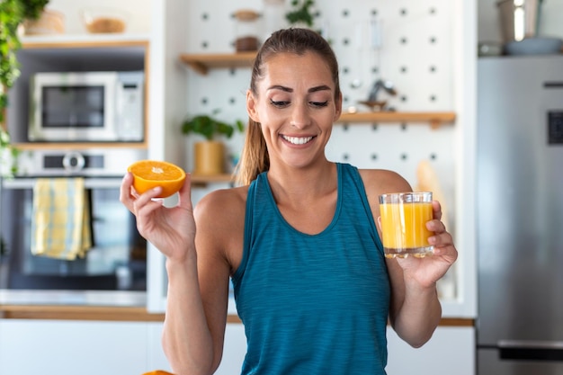 Hermosa mujer joven bebiendo jugo de naranja fresco en la cocina Dieta saludable Mujer joven feliz con un vaso de jugo y naranja en la mesa en la cocina