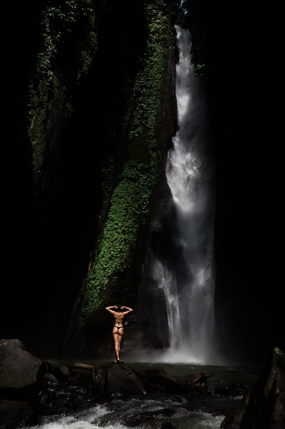 Hermosa mujer joven en bikini relajante frente a la cascada. Chica de viaje de imagen de concepto de ecoturismo