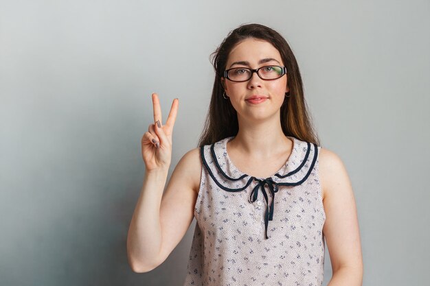 Una hermosa mujer joven con una blusa y gafas sostiene dos dedos