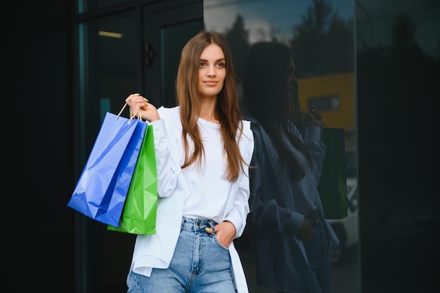 Hermosa mujer joven con bolsas de compras cerca de la tienda al aire libre