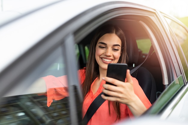 Hermosa mujer joven y bonita sonrisa y uso de teléfono móvil tocando la pantalla dentro del coche mientras viaja.