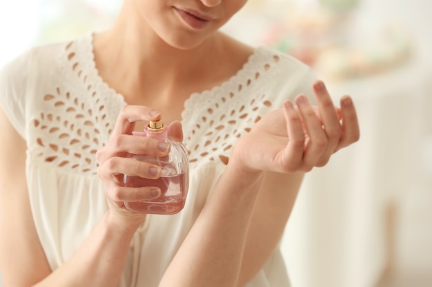 Hermosa mujer joven con botella de perfume en casa, primer plano