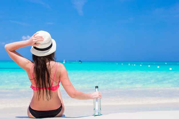 Hermosa mujer joven con botella sentado en la playa