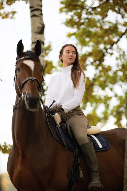 Hermosa mujer joven con caballo al aire libre Concepto de cuidado de animales Descanso y ocio rural Idea de turismo verde Joven europea en uniforme