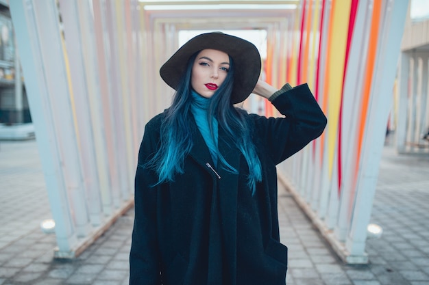 Hermosa mujer joven con cabello azul en un bonito abrigo negro, jeans y sombrero.