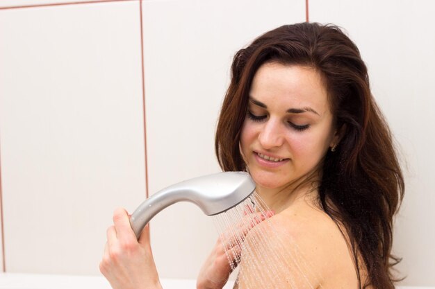 Hermosa mujer joven con cabello largo y oscuro duchándose en su baño de luz