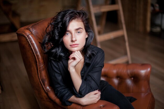 Hermosa mujer joven con cabello oscuro rizado y maquillaje natural sentada en sillas de cuero oscuro