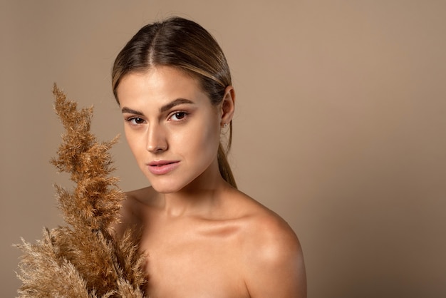 Una hermosa mujer joven con el cabello recogido sostiene una hierba de la pampa seca en sus manos. El concepto de cosmética natural a partir de granos de trigo. Protección de la piel.