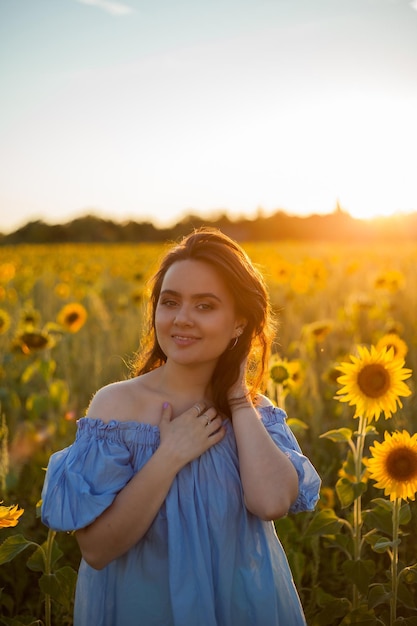 Hermosa mujer joven con cabello rizado oscuro en un campo de girasoles Modelo con un elegante vestido azul Verano cálidamente