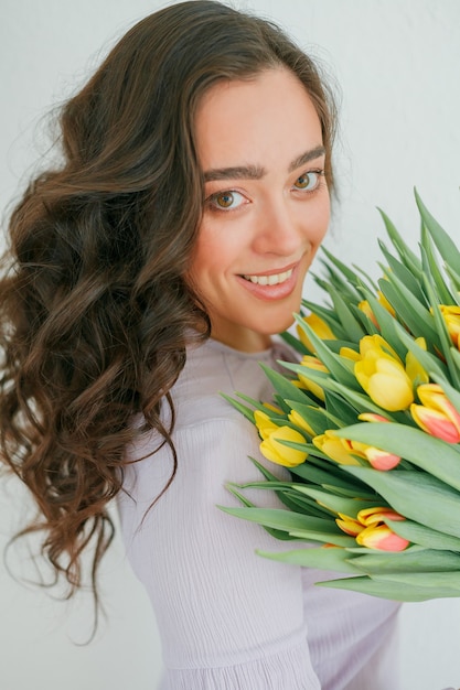 Hermosa mujer joven con cabello rizado tiene un ramo de tulipanes.