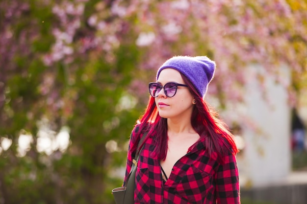 Hermosa mujer joven con cabello rosado y mirada sensual caminando por la ciudad en primavera Chica de estilo de moda con sombrero de lana púrpura y camisa de color burdeos