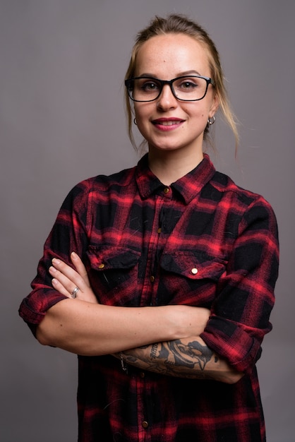 Hermosa mujer joven con cabello rubio vistiendo camisa a cuadros roja y anteojos en gris