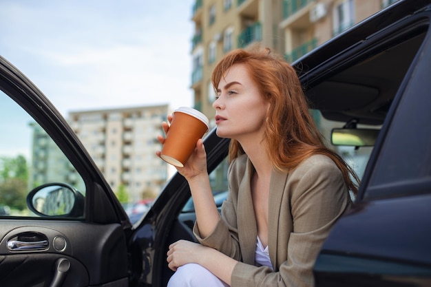 Hermosa mujer joven con café en la mano sentado en un automóvil Mujer en viaje por carretera tomando café dentro del automóvil