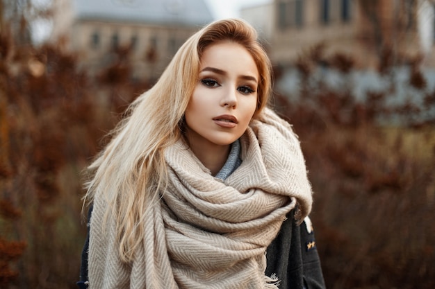 Hermosa mujer joven en una cálida bufanda de pie en el parque otoño